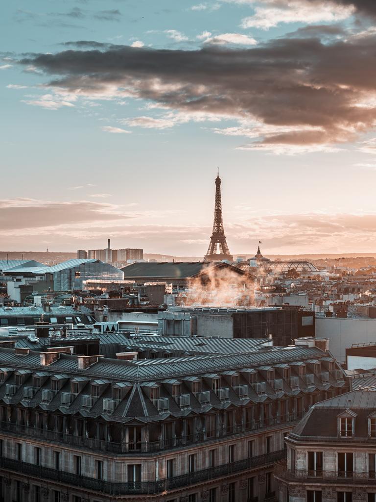 Blick über die Stadt Paris mit Eifelturm und großen Wolken bei einem diesigen Sonnenuntergang.