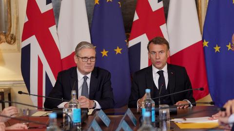 Der britische Premierminister Starmer und Frankreichs Präsident Macron sitzen nebeneinander, hinter ihnen die Landes- und die EU-Flagge.