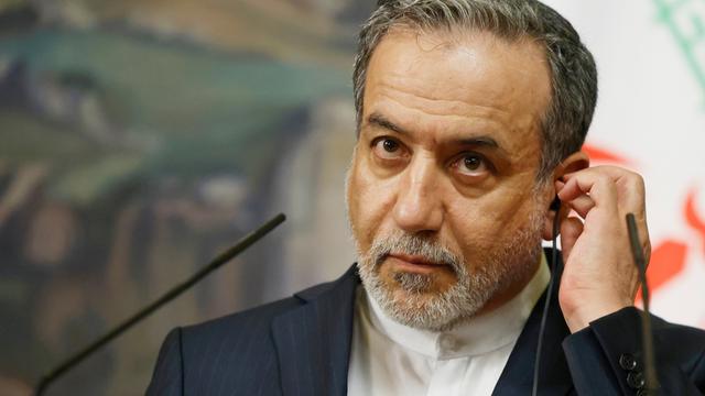 Irans Außenminister Abbas Araghtschi, vor ihm ein Mikrofon; er fasst sich mit der linken Hand ans linke Ohr.
