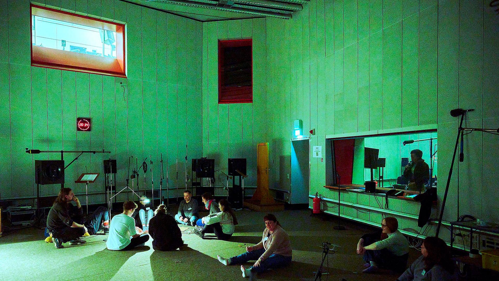 Eine Gruppe von Mensche sitzen im großen Hörspielstudio auf der Erde - Vorbereitungen zu "Making of Menschheit"
