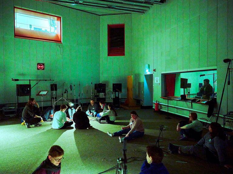 Eine Gruppe von Mensche sitzen im großen Hörspielstudio auf der Erde - Vorbereitungen zu "Making of Menschheit"