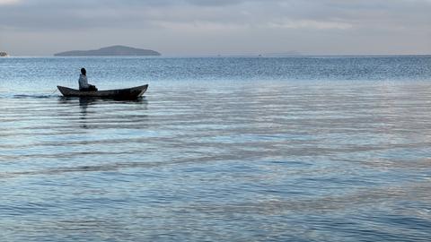 Ein Fischer auf dem Malawisee. Das Wasser ist ruhig und das kleine Boot treibt dahin.