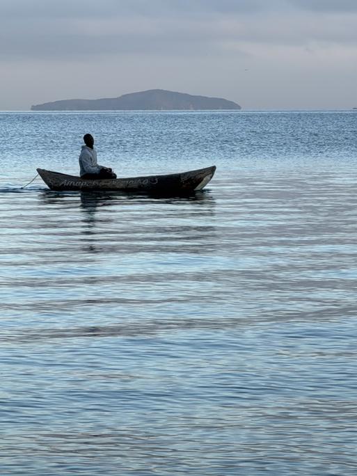 Ein Fischer auf dem Malawisee. Das Wasser ist ruhig und das kleine Boot treibt dahin.