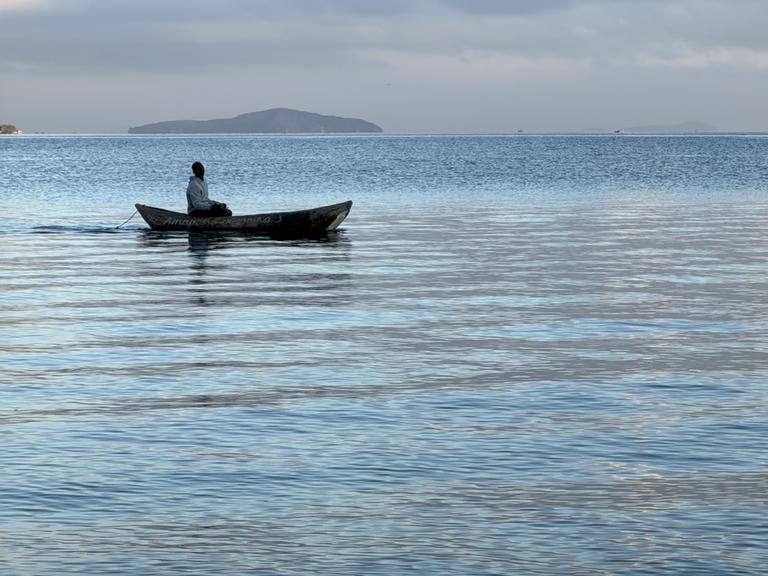Ein Fischer auf dem Malawisee. Das Wasser ist ruhig und das kleine Boot treibt dahin.