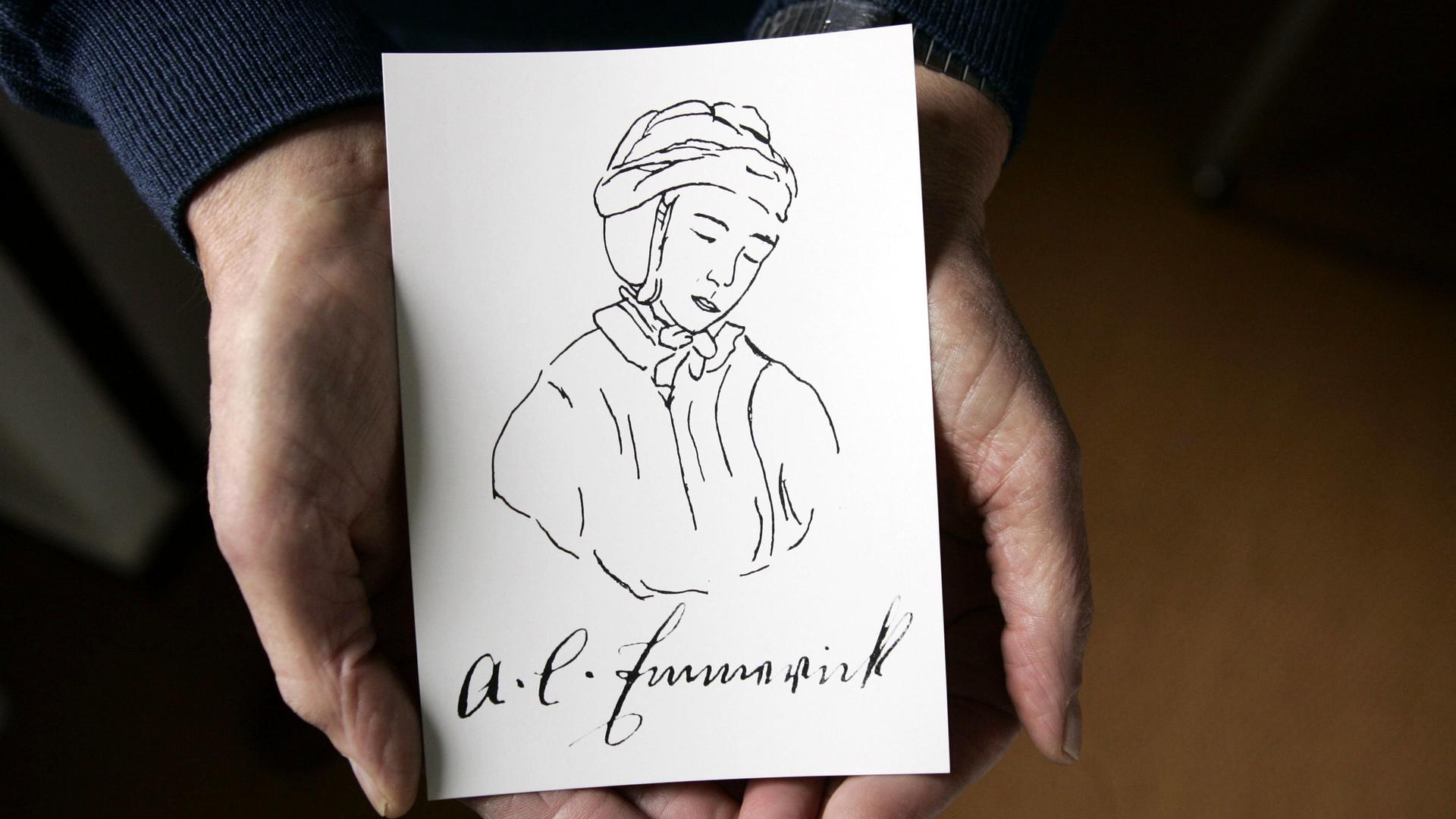 Zwei Hände halten eine Postkarte mit der Zeichnung einer Nonne. Darunter steht in Schreibschrift A.K. Emmerick.