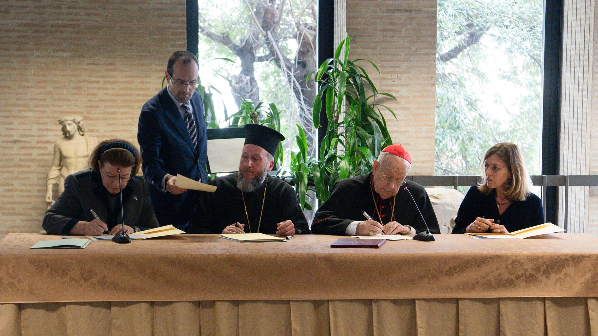 Vier Personen sitzen an einem Tisch und unterzeichnen Dokumente.