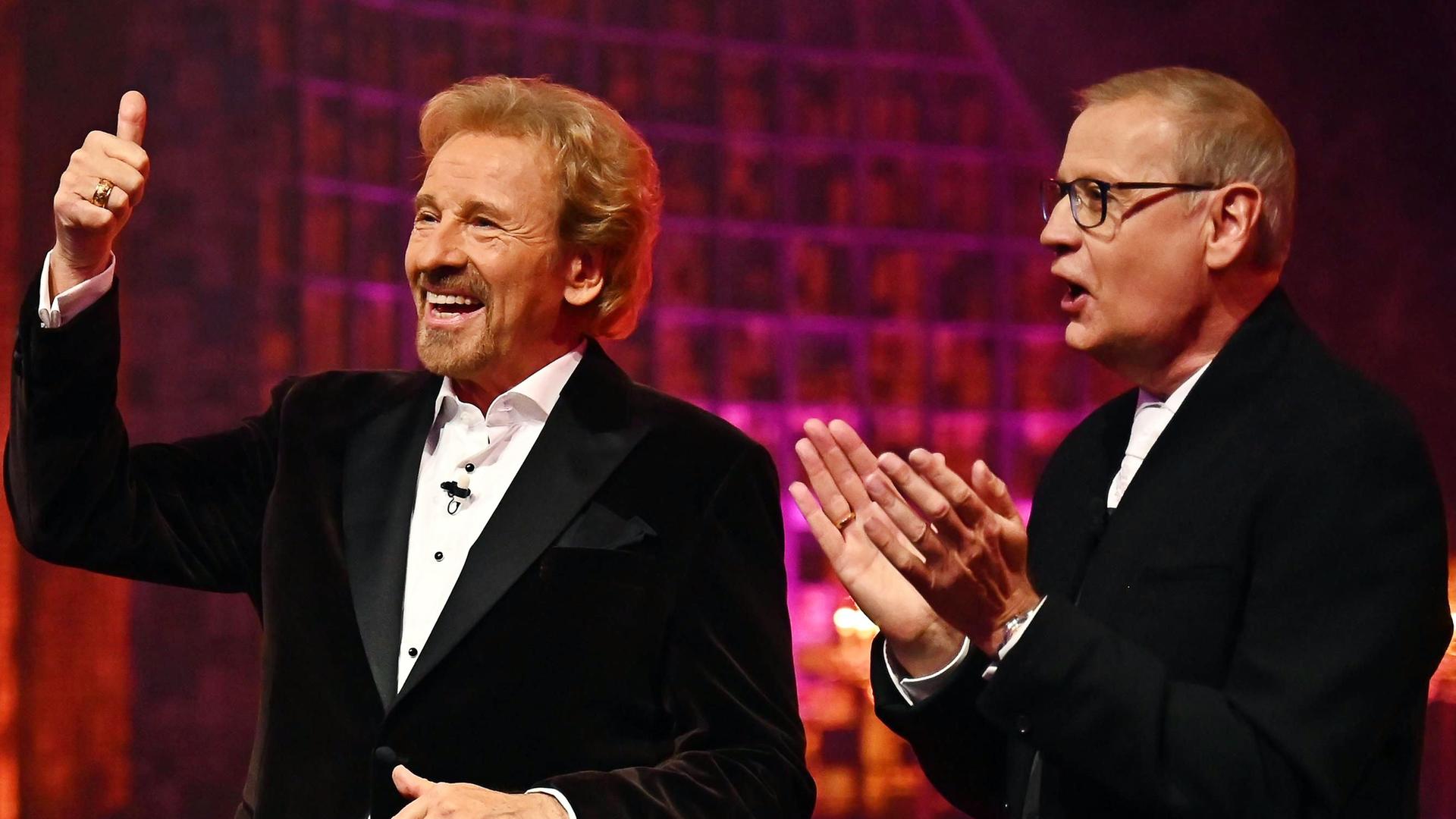 Thomas Gottschalk hält den Daumen hoch und lacht. Neben ihm steht Günther Jauch und applaudiert. Thomas Gottschalk hält den Daumen hoch und lacht. Neben ihm steht Günther Jauch und applaudiert.