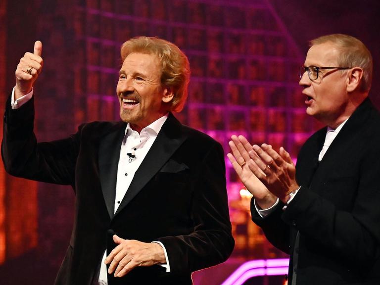 Thomas Gottschalk hält den Daumen hoch und lacht. Neben ihm steht Günther Jauch und applaudiert. 
