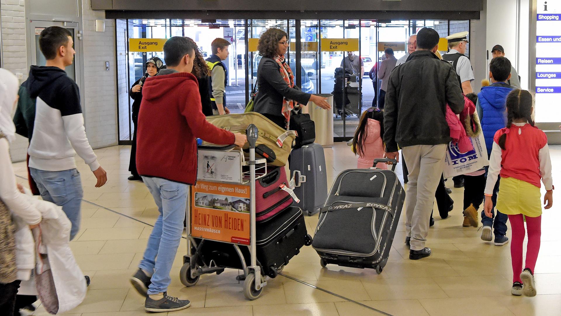 Syrische Flüchtlinge gehen mit Koffern und Taschen durch  die Ankunftshalle eines deutschen Flughafens.