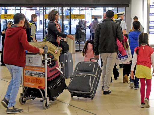 Syrische Flüchtlinge gehen mit Koffern und Taschen durch  die Ankunftshalle eines deutschen Flughafens.