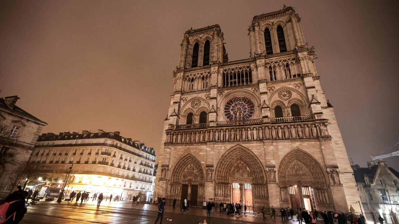 Außenansicht der zum Teil beleuchteten Kathedrale Notre-Dame in Paris. Davor stehen Menschen.