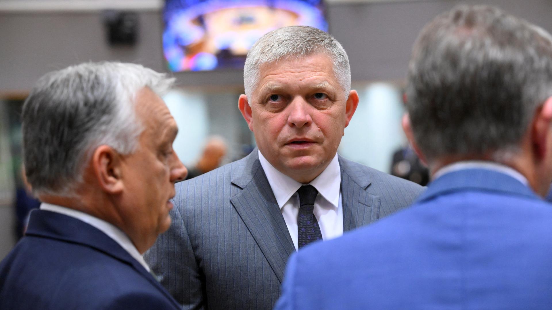 Der slowakische Premierminister Fico spricht mit dem ungarischen Ministerpräsidenten Orban, den man von der Seite sieht. Neben ihm steht ein unbekannter Mann mit dem Rücken zur Kamera. Der slowakische Premierminister Fico spricht mit dem ungarischen Ministerpräsidenten Orban, den man von der Seite sieht. Neben ihm steht ein unbekannter Mann mit dem Rücken zur Kamera.