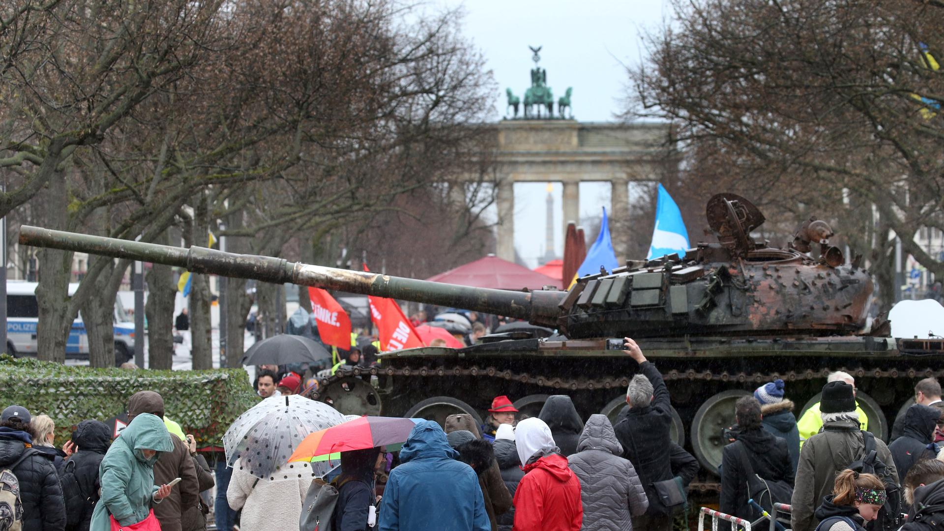 Passanten stehen vor einem in der Ukraine zerstörten russischen Panzer. Der Panzer T-72 steht auf einem Hänger vor der Botschaft Russlands Unter den Linden in Berlin. Diese Aktion soll ein Zeichen des Protests gegen den Krieg Russlands sein und soll die Solidarität mit der Ukraine ausdrücken. 