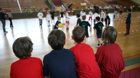 Kinder schauen beim Völkerballspiel in einer Turnhalle zu.