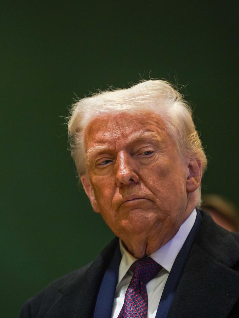 Donald Trump steht vor einer dunkelgrünen Wand und schaut nachträglich zur Seite.