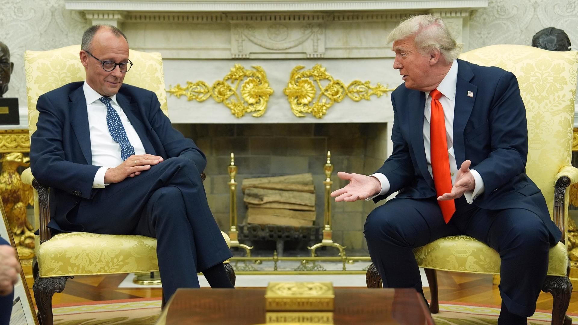 Bundeskanzler Merz und der Präsident von den USa, Donald Trump, sitzen nebeneinander auf Sesseln. Trump redet mit Merz, Merz lächelt. 