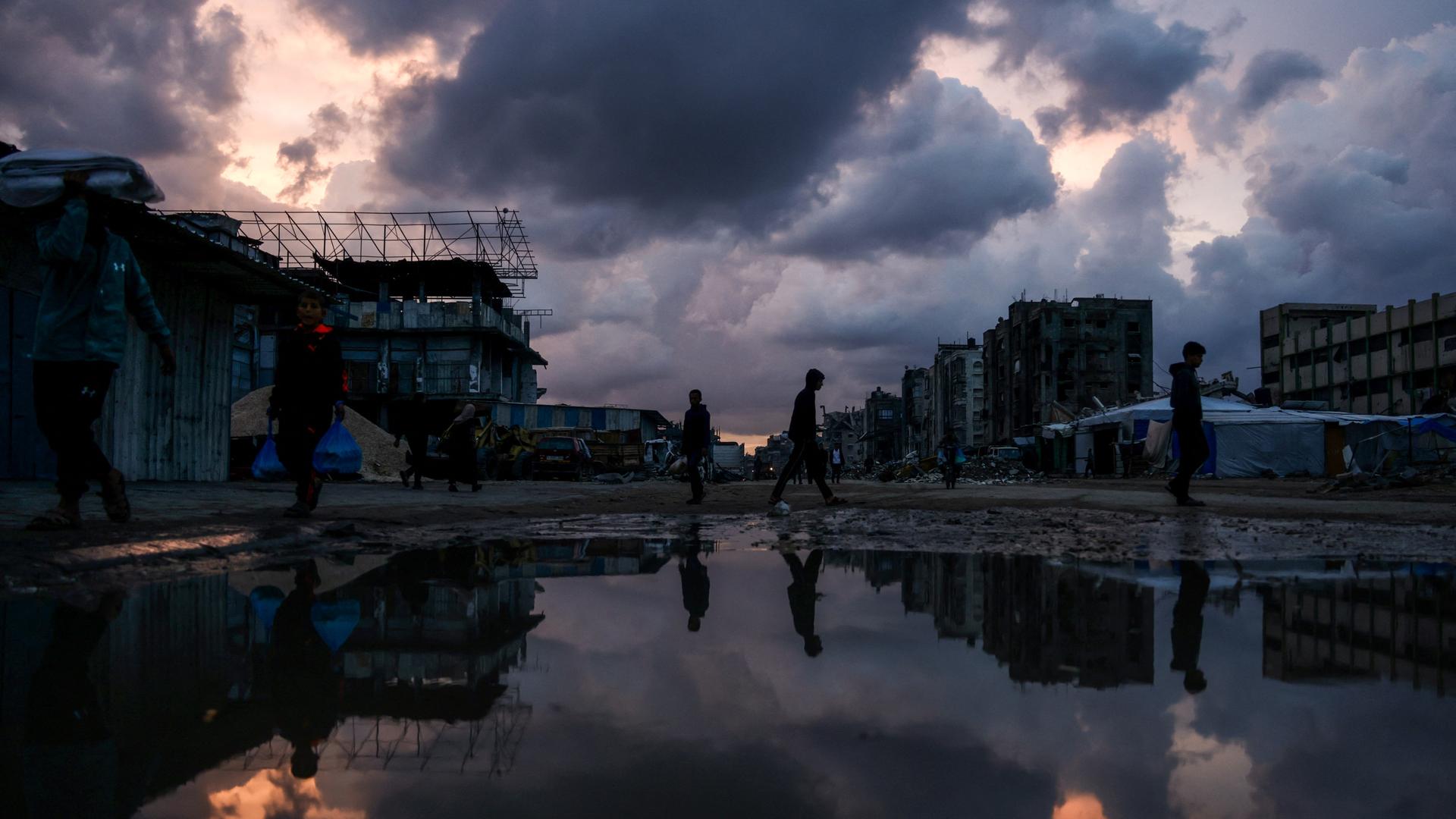 Personen gehen am 10. Dezember 2025 an einer Wasserlache im Stadtteil Al-Saftawi westlich der Stadt Jabalia im nördlichen Gazastreifen vorbei. (Photo by BASHAR TALEB / AFP) Personen gehen am 10. Dezember 2025 an einer Wasserlache im Stadtteil Al-Saftawi westlich der Stadt Jabalia im nördlichen Gazastreifen vorbei. (Photo by BASHAR TALEB / AFP)