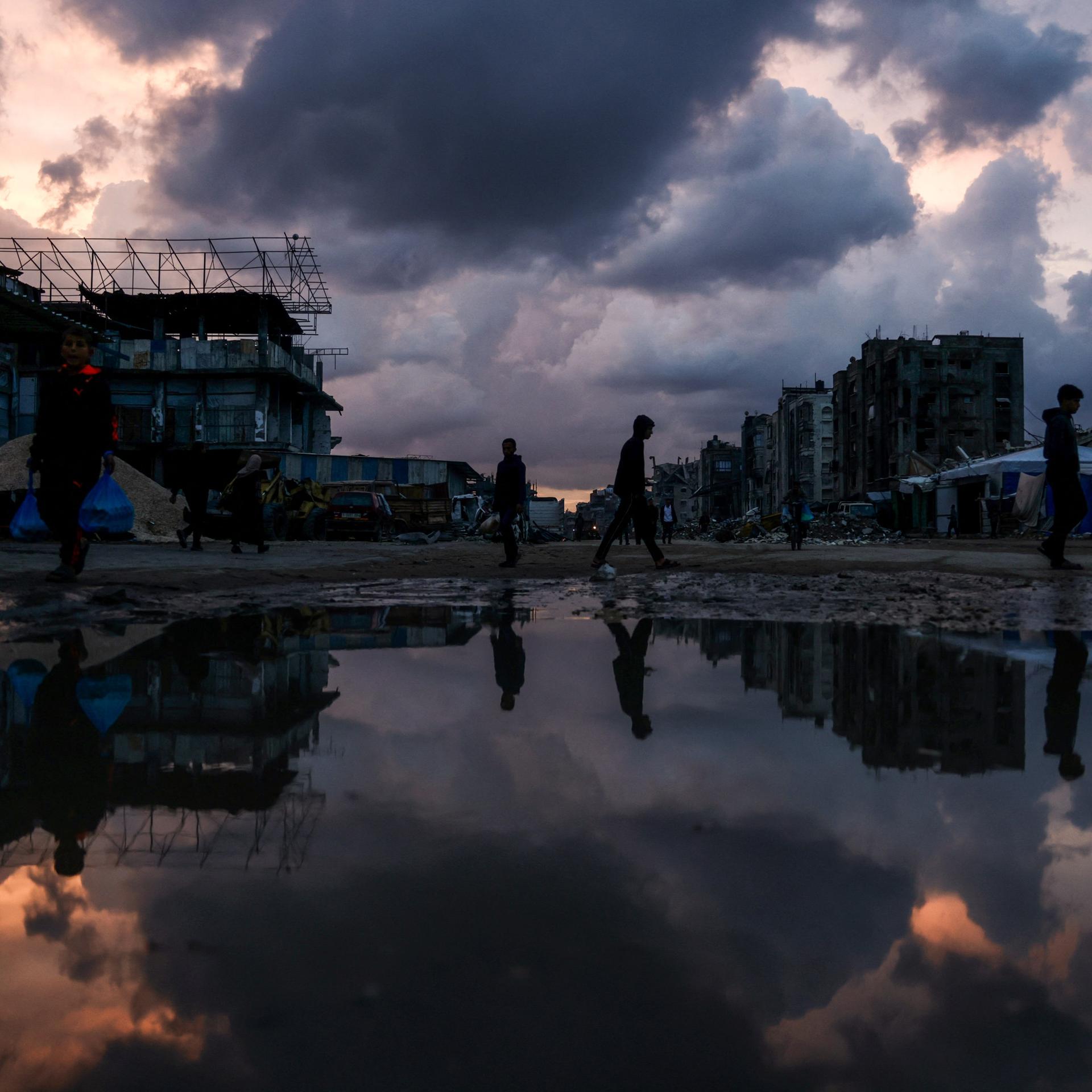Personen gehen am 10. Dezember 2025 an einer Wasserlache im Stadtteil Al-Saftawi westlich der Stadt Jabalia im nördlichen Gazastreifen vorbei. (Photo by BASHAR TALEB / AFP)