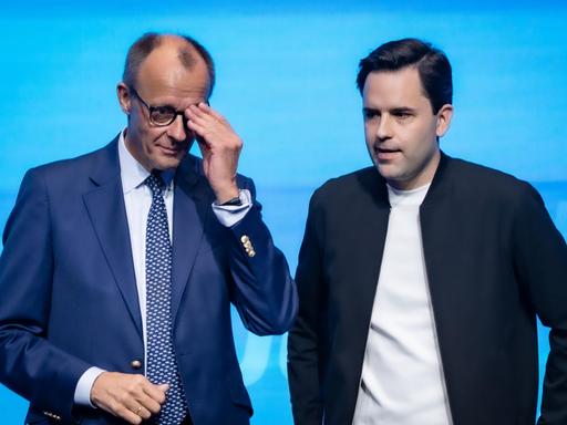 Bundeskanzler Friedrich Merz steht neben Johannes Winkel, Bundesvorsitzender Jungen Union, und fasst sich an die Brille, beide sehen nicht sehr glücklich aus Bundeskanzler Friedrich Merz steht neben Johannes Winkel, Bundesvorsitzender Jungen Union, und fasst sich an die Brille, beide sehen nicht sehr glücklich aus
