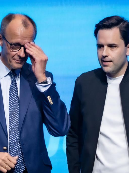 Bundeskanzler Friedrich Merz steht neben Johannes Winkel, Bundesvorsitzender Jungen Union, und fasst sich an die Brille, beide sehen nicht sehr glücklich aus Bundeskanzler Friedrich Merz steht neben Johannes Winkel, Bundesvorsitzender Jungen Union, und fasst sich an die Brille, beide sehen nicht sehr glücklich aus