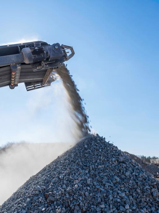 Geschredderte Betonbrocken fallen von einem Förderband auf einen kegelförmigen Haufen