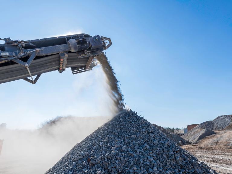 Geschredderte Betonbrocken fallen von einem Förderband auf einen kegelförmigen Haufen