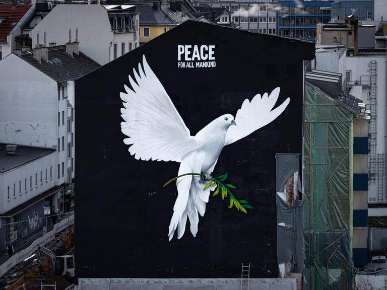 „PEACE FOR ALL MANKIND“ („Frieden für die ganze Menschheit“) steht über dem Bild einer riesigen Friedenstaube an einer Hauswand in Frankfurt am Main. „PEACE FOR ALL MANKIND“ („Frieden für die ganze Menschheit“) steht über dem Bild einer riesigen Friedenstaube an einer Hauswand in Frankfurt am Main.