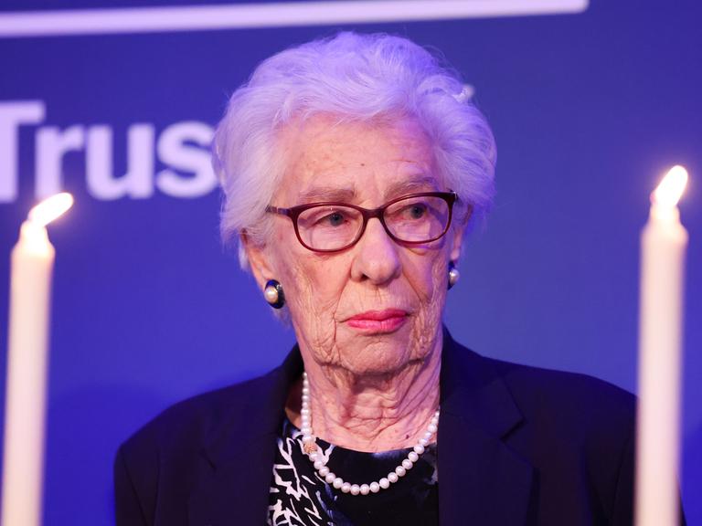 Eva Schloss schaut ernst zur Seite. Neben ihr leuchten Kerzen. 