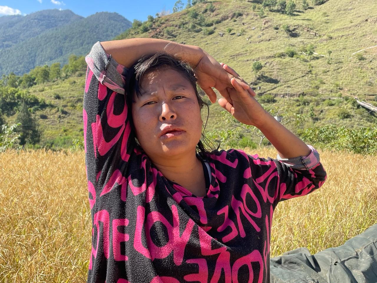 Eine Frau in schwarzem T-Shirt mit pink Buchstaben schlingt sich vor Bergpanorama die Arme um den Kopf.