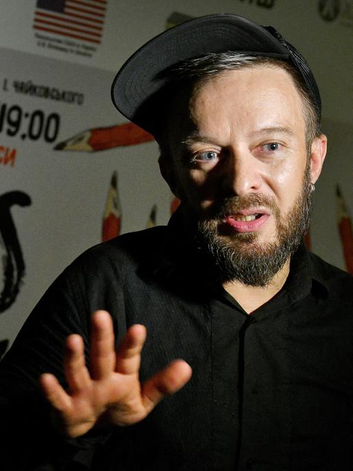 Der ukrainische Theatermacher Pavlo Arie, ein Mann mittleren Alters mit Bart und einem Basecap, gestikuliert im Gespräch mit seiner Hand.