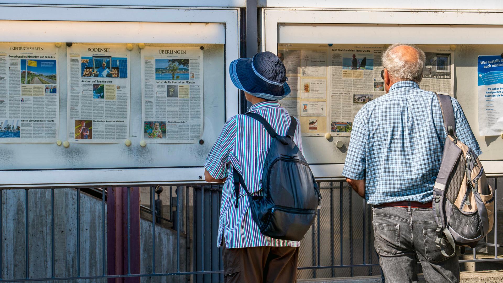 Zwei ältere Zeitungsleser stehen vor einem Aushang des "Südkurier" aus Überlingen