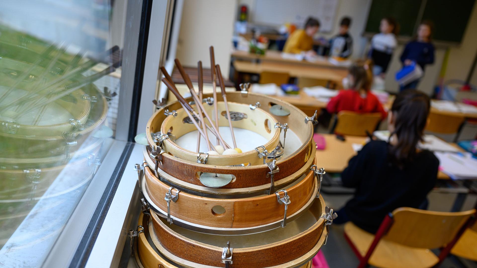 Tamburine liegen auf der Fensterbank in einer Grundschule, im Hintergrund sind verschwommen Pulte, Tafel und Kinder zu sehen. Tamburine liegen auf der Fensterbank in einer Grundschule, im Hintergrund sind verschwommen Pulte, Tafel und Kinder zu sehen.