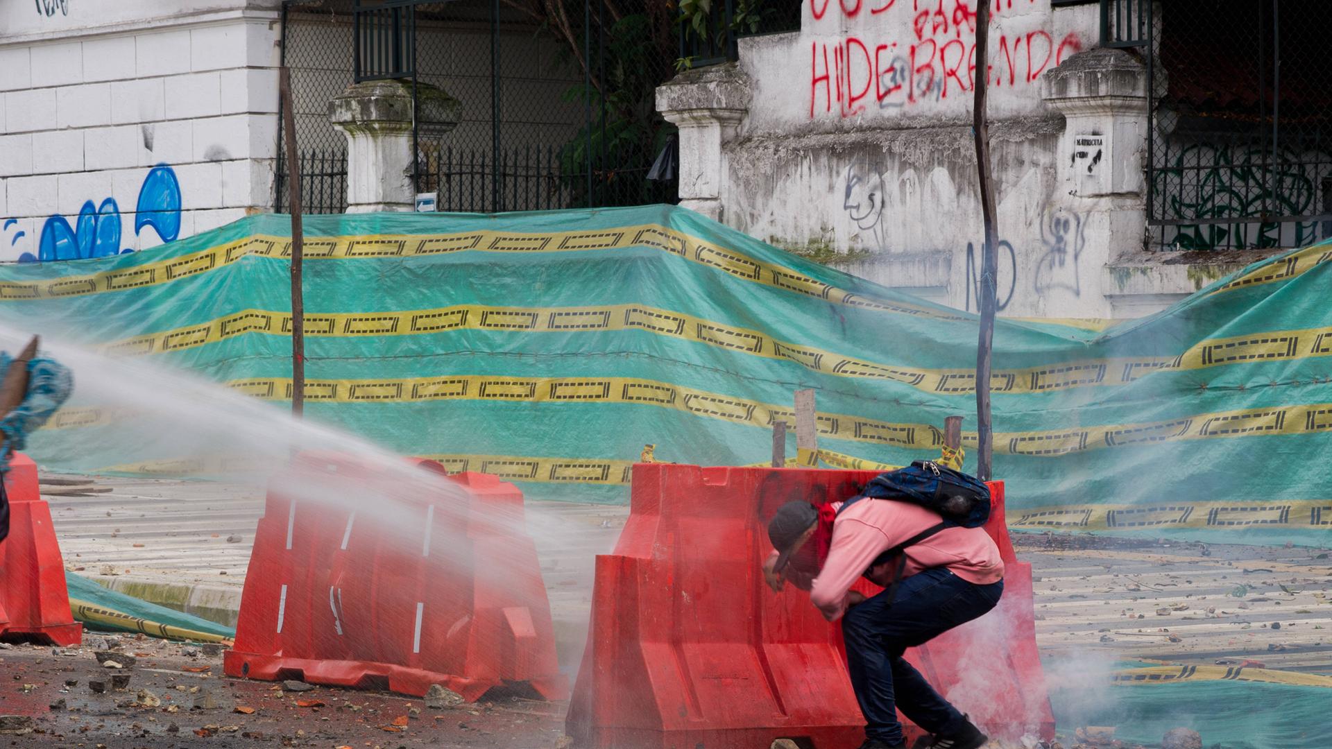 Demonstration In Bogota, Colombia Erupts In Clashes A demonstrator takes cover behind a road barrier as it s hit by a wa