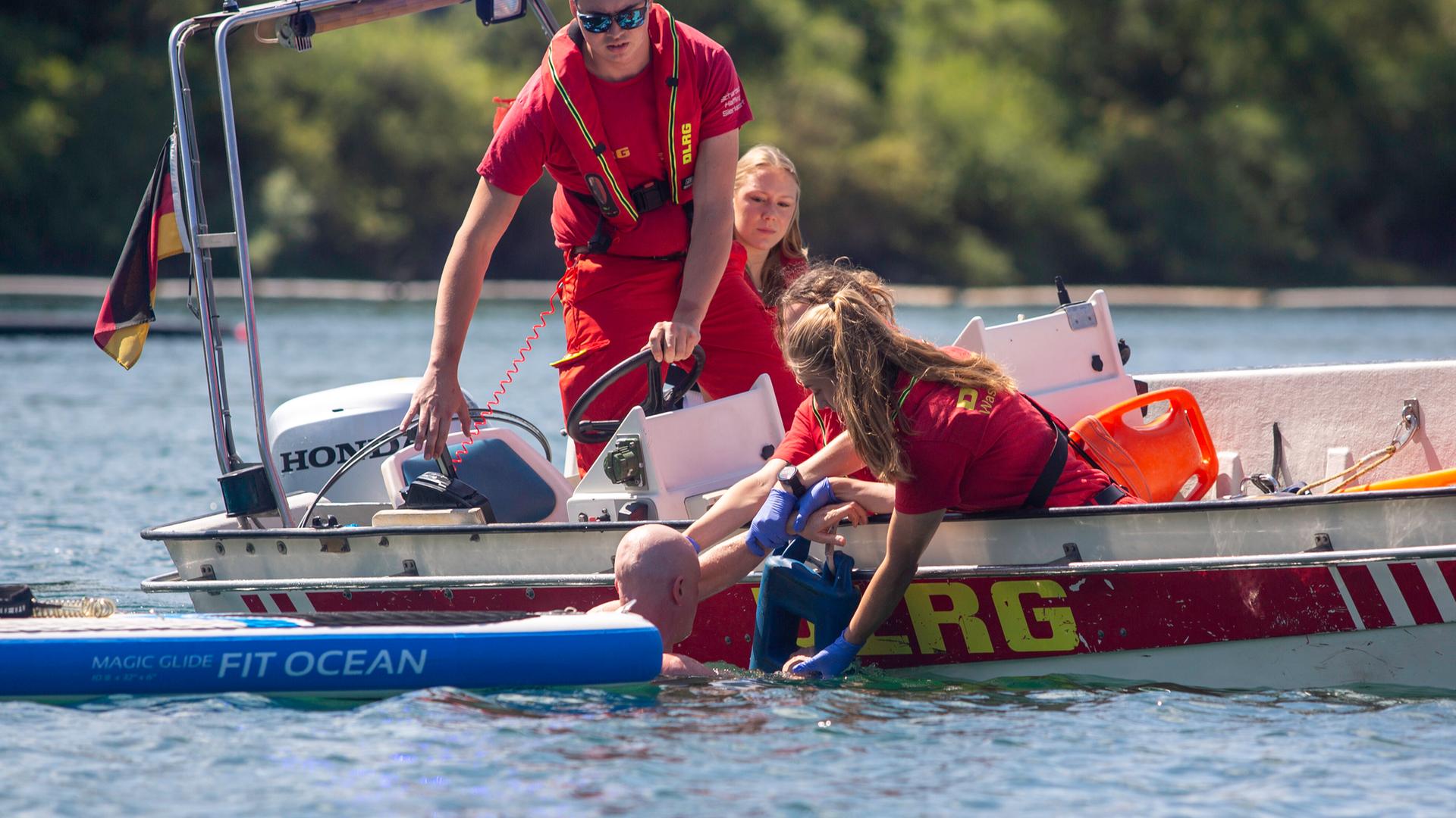 Einsatzkräfte von DLRG und Feuerwehr ziehen von einem Boot aus einen glatzköpfigen Mann aus dem Wasser.