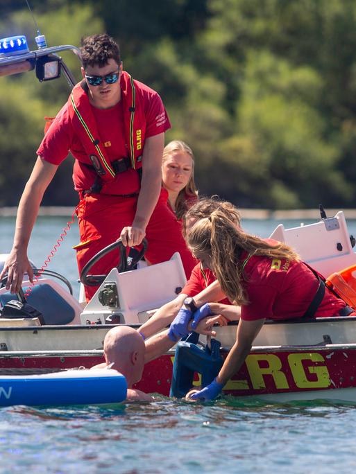 Einsatzkräfte von DLRG und Feuerwehr ziehen von einem Boot aus einen glatzköpfigen Mann aus dem Wasser.