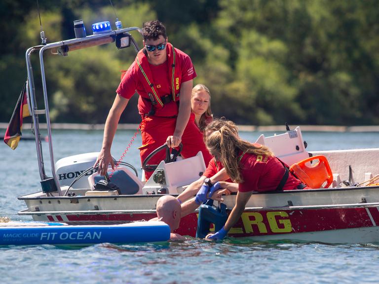 Einsatzkräfte von DLRG und Feuerwehr ziehen von einem Boot aus einen glatzköpfigen Mann aus dem Wasser.