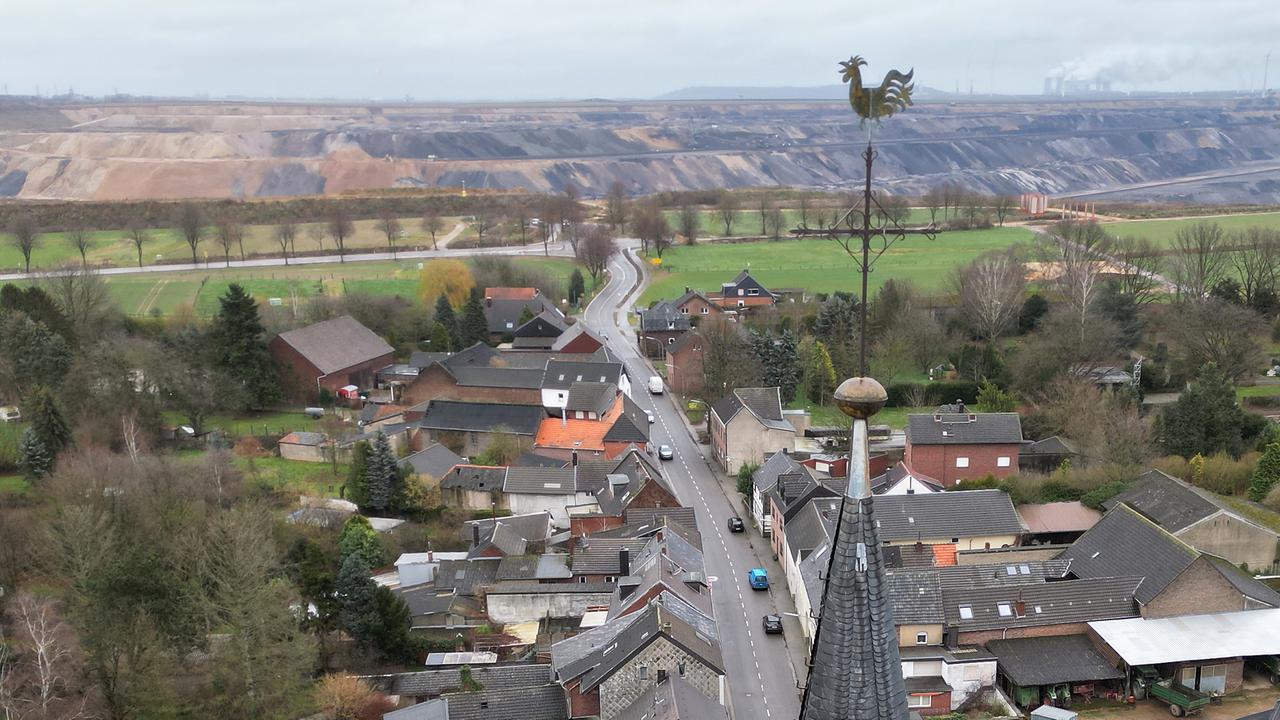 Eine Luftaufnahme des Dorfes Keyenberg: Im Vordergrund sieht man eine Kirchturmspitze, unten stehen mehrere Häuser entlang einer Dorfstraße. Nach kurzer Entfernung sieht die Abbruchkante des Tagebaus Garzweiler. 