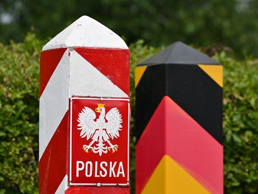 Ein Grenzpfeiler in den polnischen Nationalfarben und einen deutscher Grenzpfeiler stehen eng nebeneinander. 