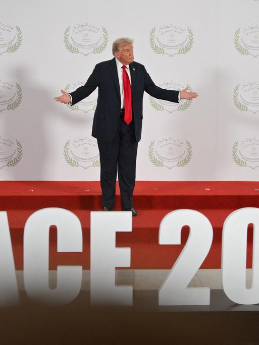 Donald Trump steht im ägyptischen Küstenort Scharm el-Scheich bei der Unterzeichnung des Abkommens für Gaza auf einer Bühne und breitet die Arme aus. Am Fuß der Bühne ist "Peace 2025" zu lesen. 