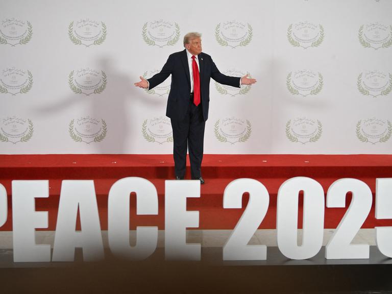 Donald Trump steht im ägyptischen Küstenort Scharm el-Scheich bei der Unterzeichnung des Abkommens für Gaza auf einer Bühne und breitet die Arme aus. Am Fuß der Bühne ist "Peace 2025" zu lesen. 