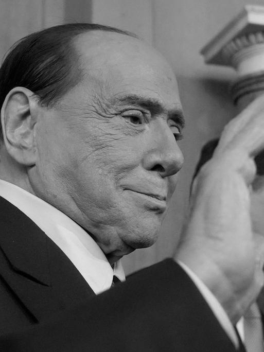 Ein schwarz-weiß Foto von Silvio Berlusconi, ehemaligem Ministerpräsidenten von Italien, er winkt Journalisten.