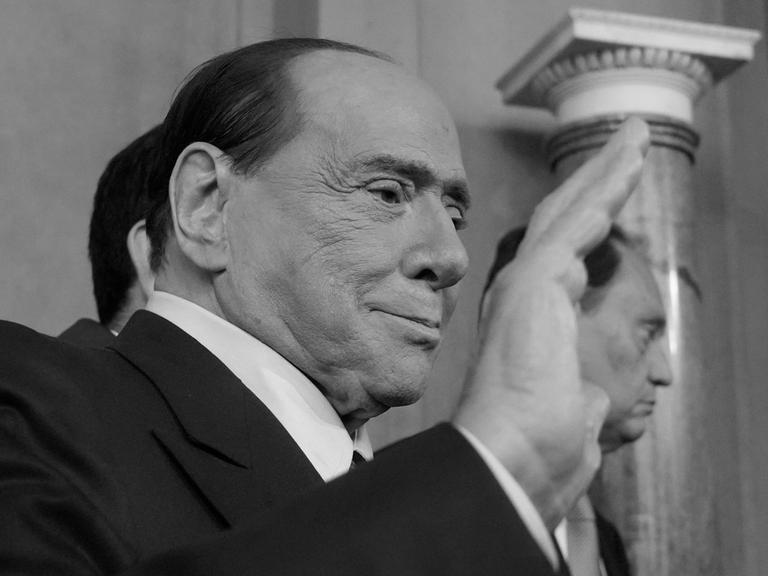 Ein schwarz-weiß Foto von Silvio Berlusconi, ehemaligem Ministerpräsidenten von Italien, er winkt Journalisten.
