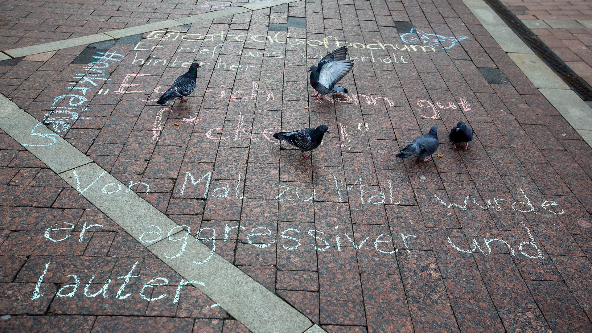 Einige Tauben stehen am Donnerstag, dem 8. April 2021 in der Füßgängerzone nahe Husemannplatz in Bochum auf dem mit Straßenmalkreide erstellten Sprüchen von sexuellen Belästigungen durch Männer. 