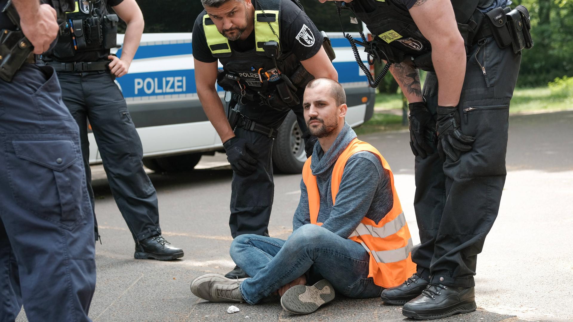 Polizisten sprechen mit einem Mann, der im Schneidersitz auf einer Straße in Berlin sitzt.