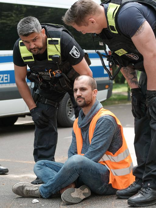 Polizisten sprechen mit einem Mann, der im Schneidersitz auf einer Straße in Berlin sitzt.