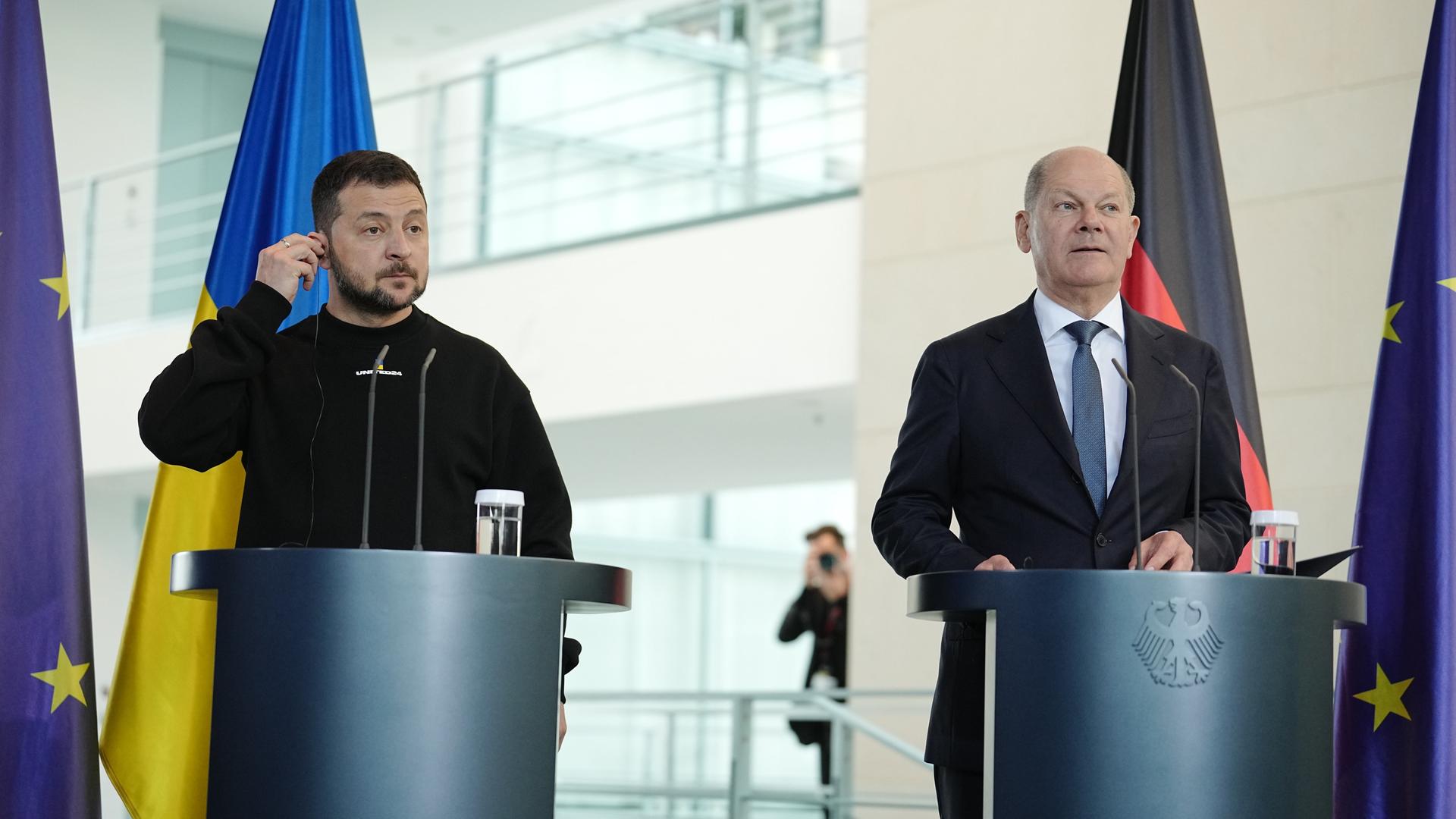 Der ukrainische Präsident Selenskyj und Bundeskanzler Scholz bei einer Pressekonferenz in Berlin. Beide stehen an Rednerpulten vor Flaggen Deutschlands, der Ukraine und der Europäischen Union. Der ukrainische Präsident Selenskyj und Bundeskanzler Scholz bei einer Pressekonferenz in Berlin. Beide stehen an Rednerpulten vor Flaggen Deutschlands, der Ukraine und der Europäischen Union.