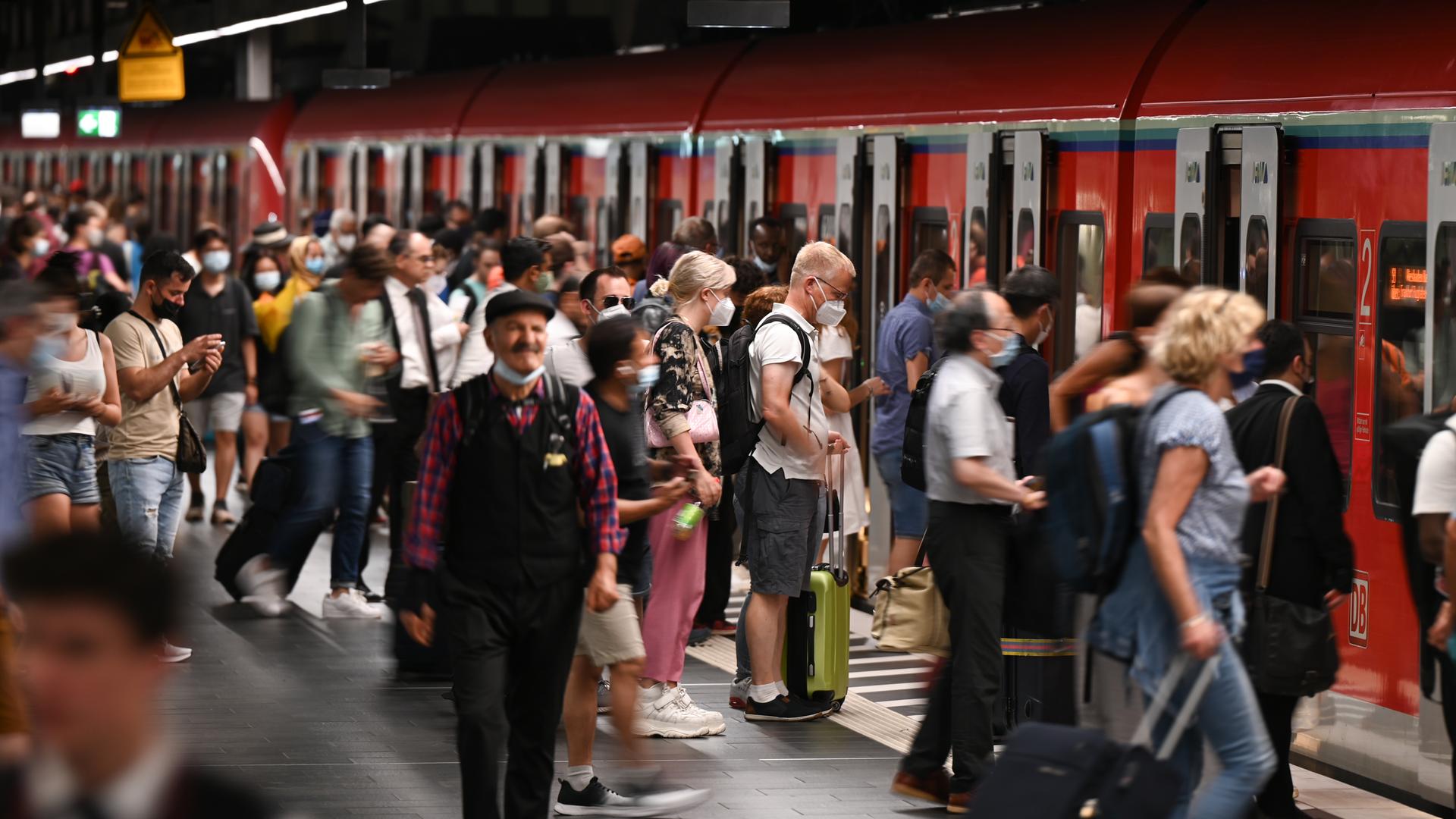 Zugreisende auf einem vollen Bahngleis, einige steigen in eine S-Bahn ein.  