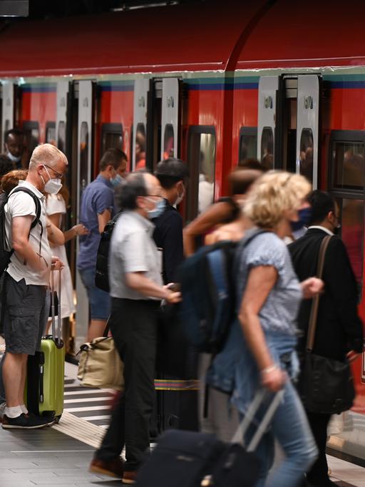 Zugreisende auf einem vollen Bahngleis, einige steigen in eine S-Bahn ein.  