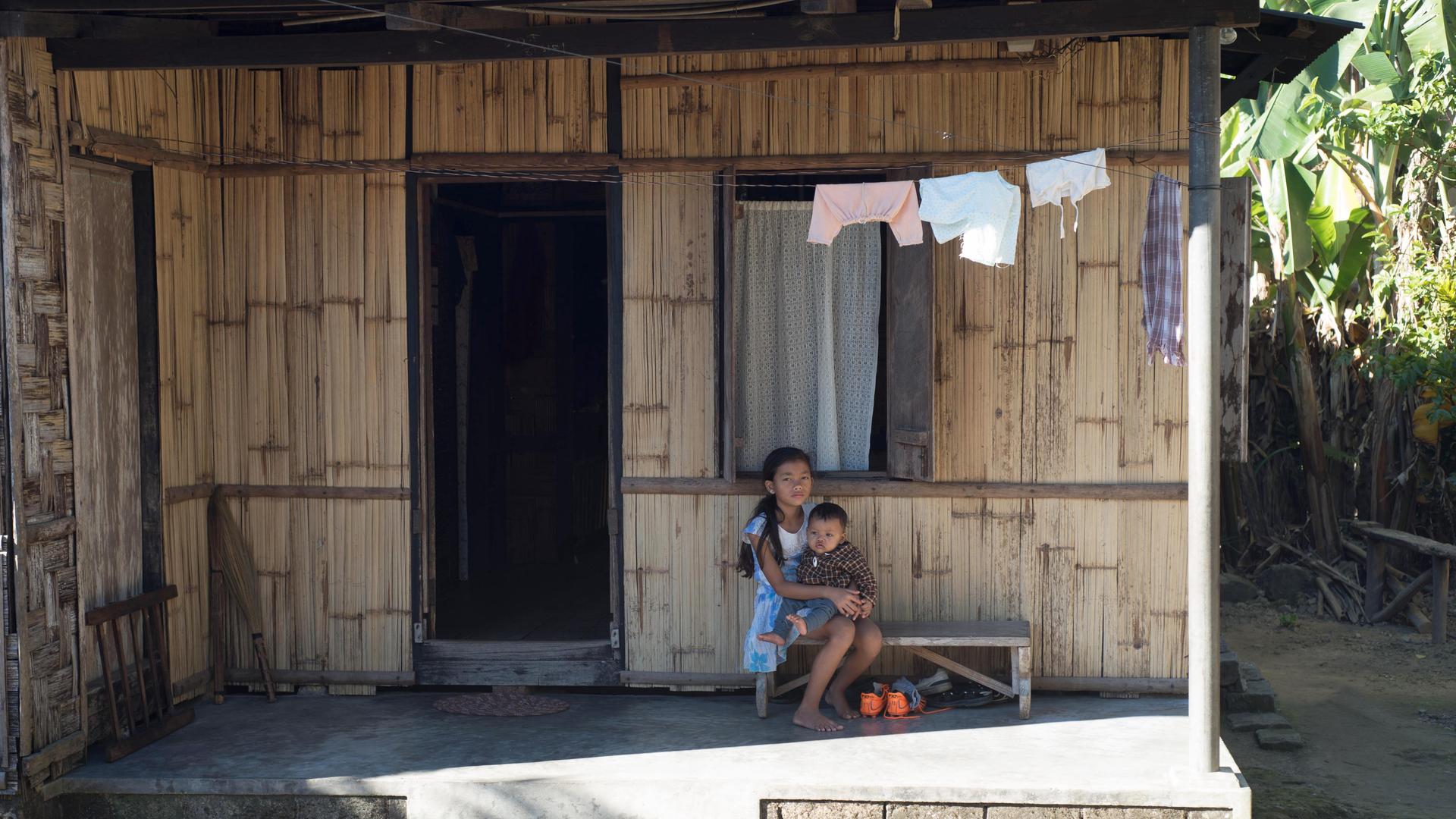 Zwei Kinder sitzen auf der Veranda eines Hauses aus Bambus und Stein in Indien.