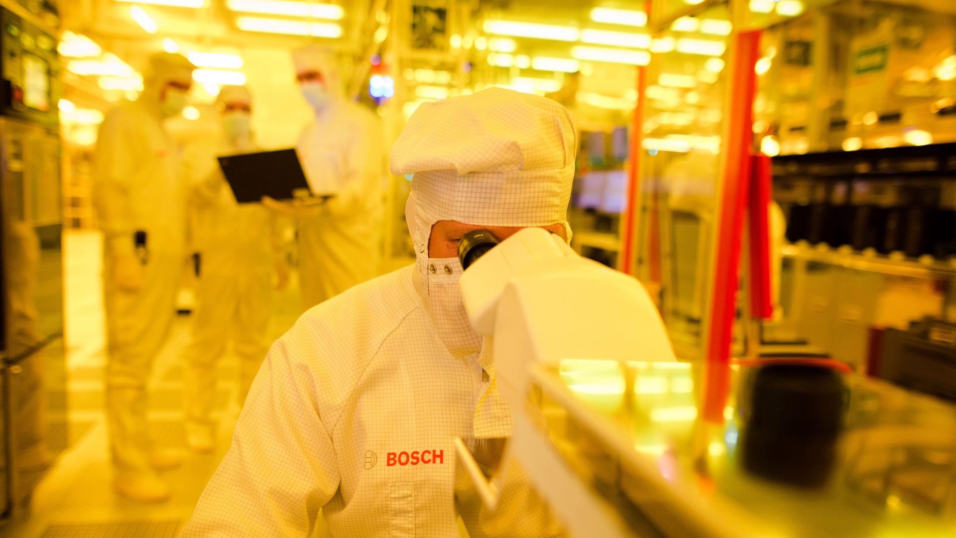 Ein Mitarbeiter von Bosch kontrolliert in einem Gelbraum in Reutlingen (Baden-Württemberg) eine Halbleiterscheibe mit einem Mikroskop auf mögliche Fehler. Ein Mitarbeiter von Bosch kontrolliert in einem Gelbraum in Reutlingen (Baden-Württemberg) eine Halbleiterscheibe mit einem Mikroskop auf mögliche Fehler.